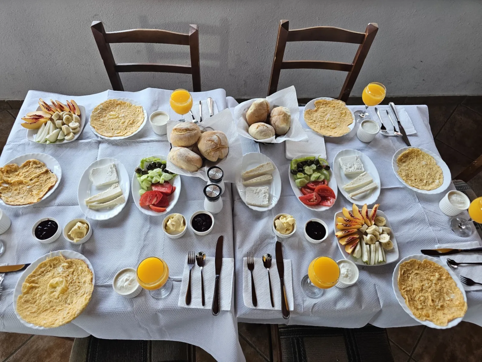 Breakfast for four: omelettes, white cheese, tomatoes, cucumbers, olives, bread rolls, fruit, yoghurt, jam and orange juice