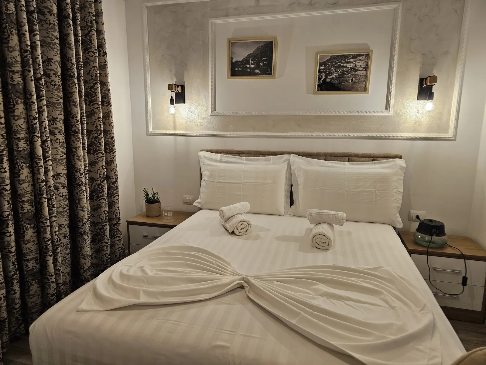 Double room with white striped linen, rolled towels and two wall lamps